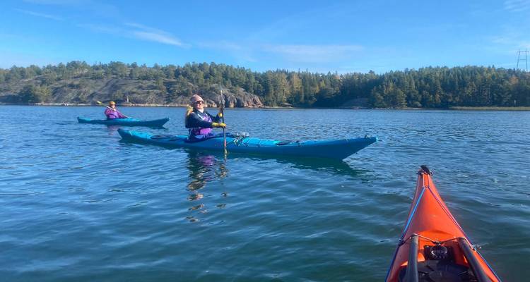Dos kayakistas reman a través de aguas azules y tranquilas rodeadas de islas boscosas bajo un cielo despejado.
