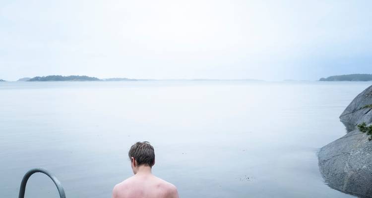 Vista trasera de un hombre preparándose para sumergirse en agua helada en un mar nórdico gris y brumoso.