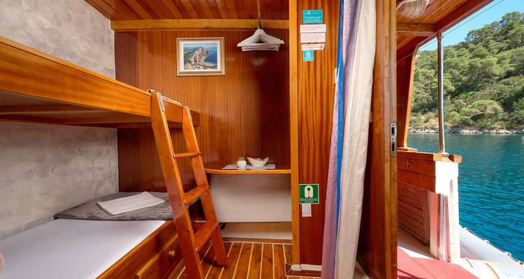 Interior de una habitación de camarote en un barco con literas y decoración náutica.