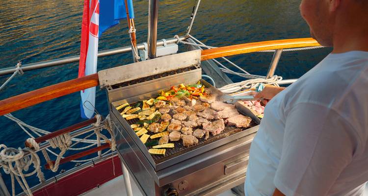 Persona asando comida en un barco con vista al mar.