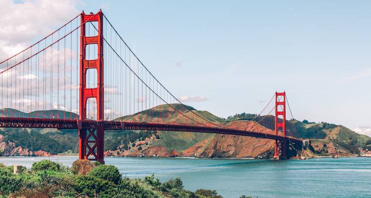 Icónico Puente Golden Gate que se extiende sobre aguas turquesas con colinas verdes ondulantes bajo un cielo despejado.