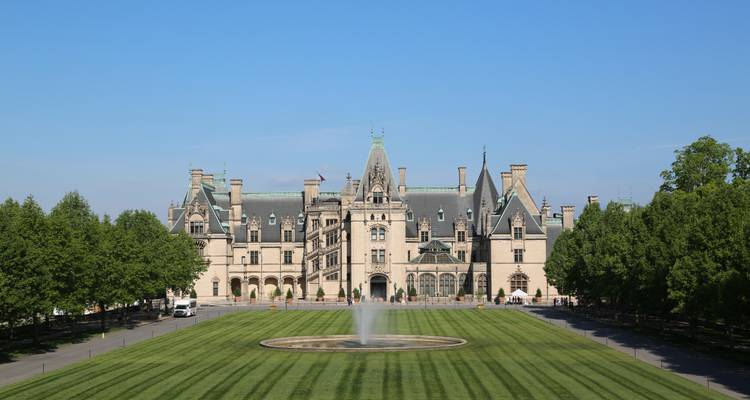 Biltmore Estate mansion framed by symmetrical trees and fountain on a bright clear day.