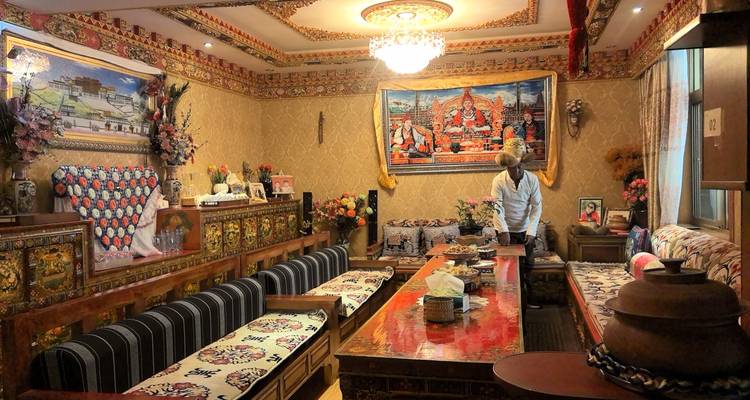 Traditional Tibetan-style living room richly decorated with tapestries, carvings and a chandelier while a host prepares tea.
