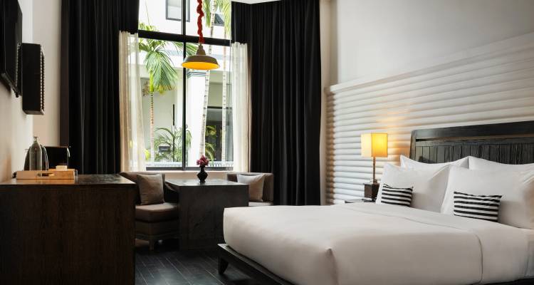 Chambre d'hôtel moderne et élégante avec un grand lit, un coin salon et de grandes fenêtres donnant sur une végétation tropicale.