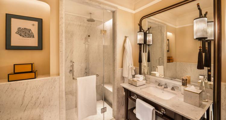 Baño de mármol lujoso con ducha de vidrio, toallas suaves y elegante tocador de lavabo bajo una iluminación cálida.