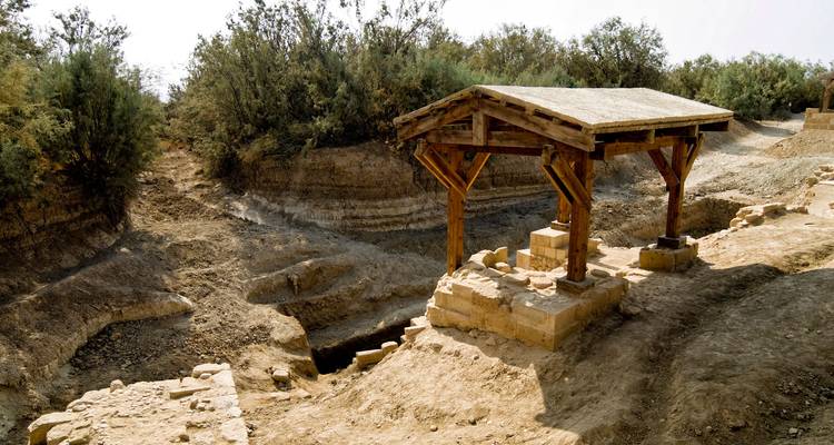 Einfaches Holzschutzdach markiert die historische Taufstelle inmitten trockenen, sandigen Geländes.