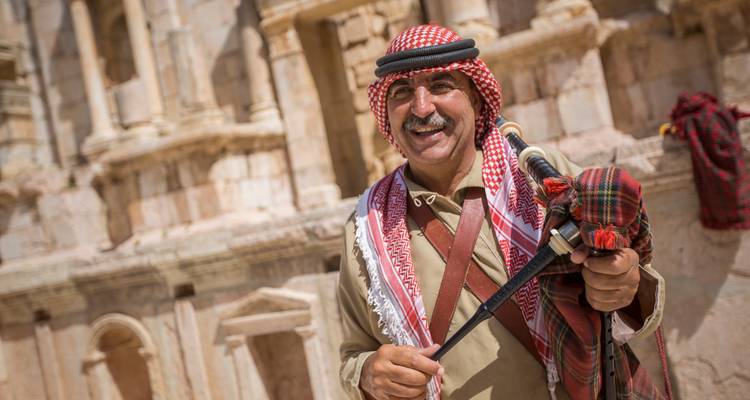 Lächelnder Beduine in traditionellem rotem Keffiyeh posiert mit einem Schwert bei antiken Ruinen.