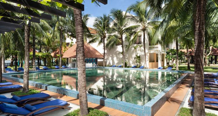Tropical resort swimming pool lined with blue loungers, palm trees and sunny skies.