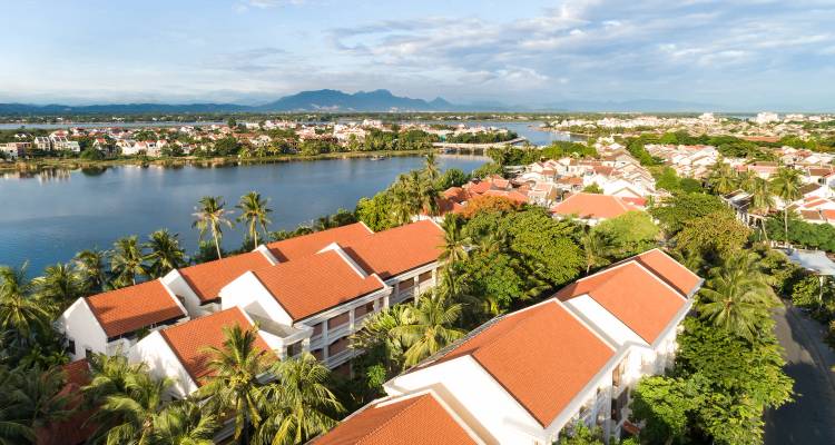 Aerial view of orange-roofed town beside a calm river with distant mountains.