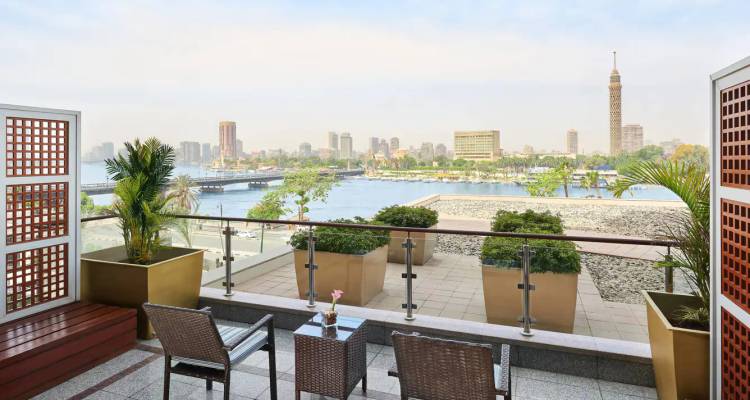 Riverside hotel balcony overlooking the Nile with Cairo Tower and city skyline in hazy light.