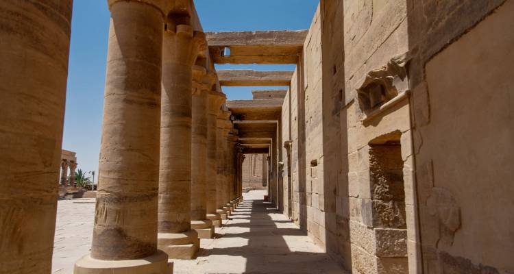 Sandstone colonnade of an ancient Egyptian temple with deep shadows and blue sky above.