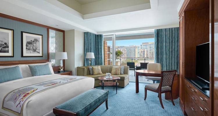 Elegant hotel room with king bed, seating area and balcony overlooking modern Cairo buildings.