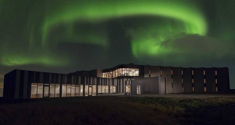 Edificio de hotel moderno iluminado bajo las auroras boreales verdes girando en el cielo oscuro.