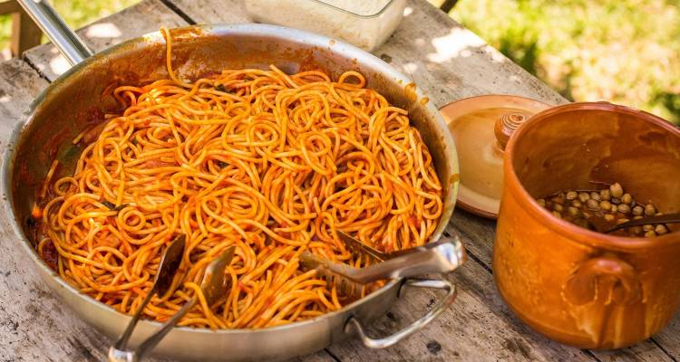 Rustic outdoor table with pan of tomato spaghetti and clay pot of beans
