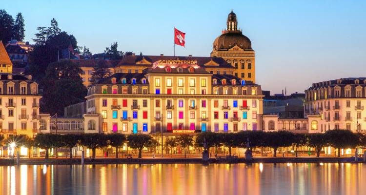 Elegant lakeside Hotel Schweizerhof illuminated at dusk reflecting on water