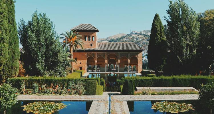 Lush Islamic garden with reflecting pools and arched pavilion framed by cypress trees