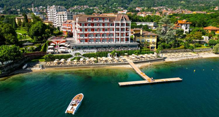 Hotel elegante a orillas del lago con fachada roja, playa privada y embarcadero visto desde arriba en el Lago Mayor.