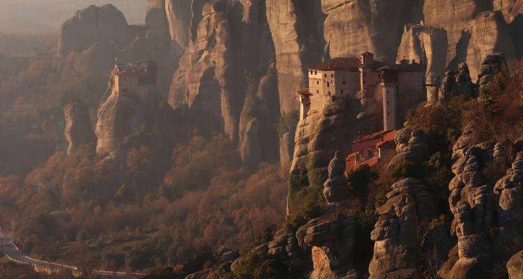 Monasteries perched atop dramatic sandstone pillars in the mountains of Meteora during warm light