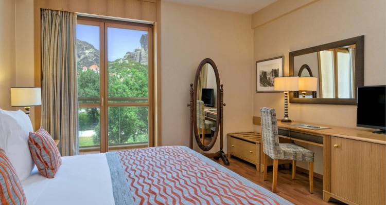 Comfortable hotel bedroom with patterned bedspread, desk and view of Meteora rocks through window