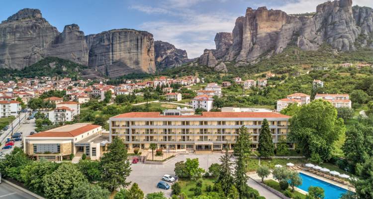 Aerial view of large hotel complex with pool in town beneath towering Meteora rock formations