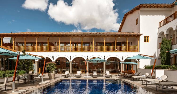 Luxurious courtyard pool bordered by arched colonial architecture under blue skies.