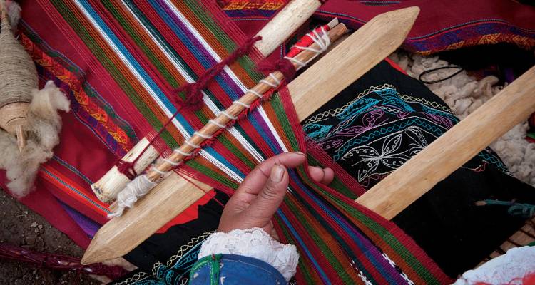 Primer plano de una mano tejiendo coloridos textiles andinos en un telar tradicional.
