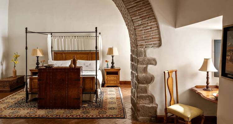 Suite amplia de estilo colonial con cama con dosel, arco de piedra y decoración de muy buen gusto.