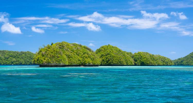 Lush green limestone islets rise from vivid turquoise water under a bright blue tropical sky.