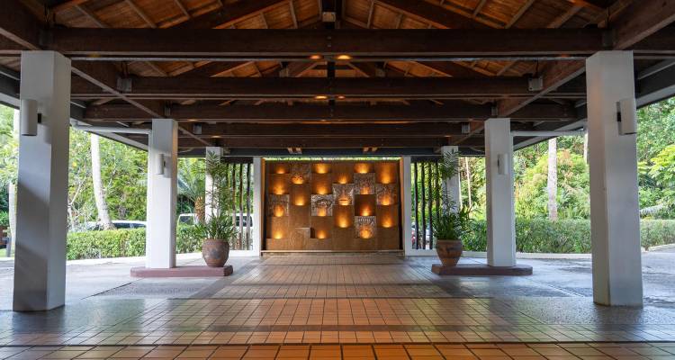 Open-air hotel lobby entrance with tiled floor, wooden beams and decorative illuminated wall