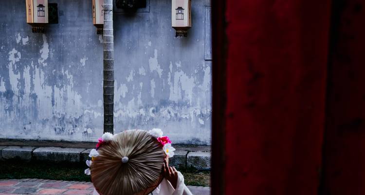 Cadre artistique d'une personne en costume traditionnel partiellement cachée derrière une porte rouge.