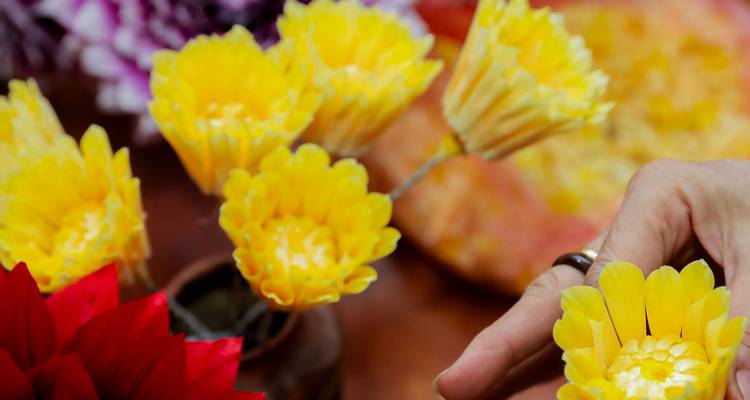 Des mains confectionnent des fleurs en papier jaune vif pour une décoration traditionnelle.