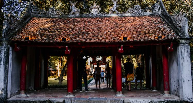 Los visitantes caminan bajo el techo de tejas y los pilares rojos de la entrada de un santuario histórico.