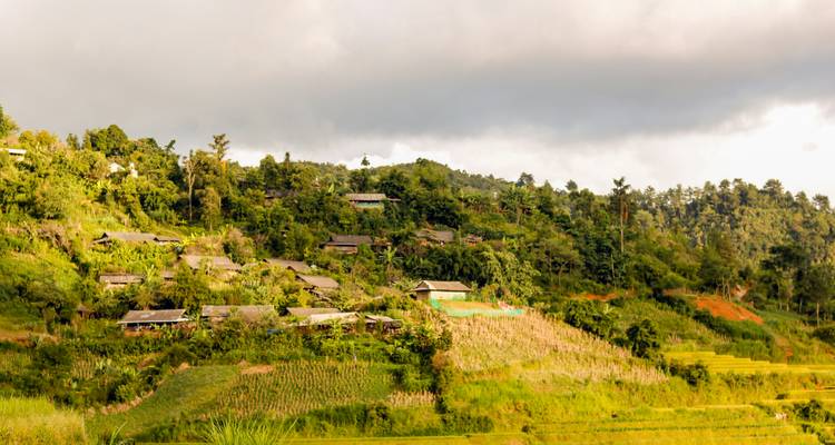 Ladera rural salpicada de casitas y campos de retazos bajo un cielo nublado.