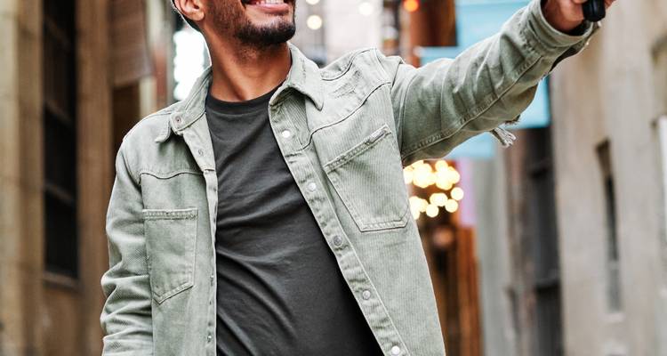 Young man takes a cheerful selfie in a narrow urban alley lined with lights.