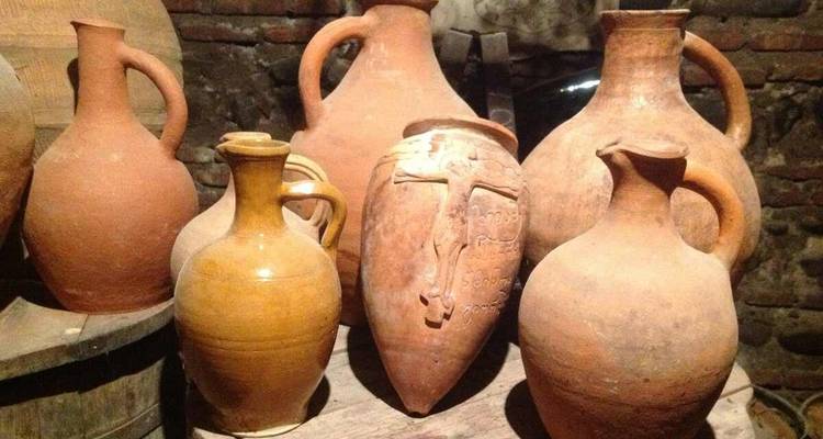 Collection of rustic Georgian clay wine jugs arranged on a wooden table inside a cellar.