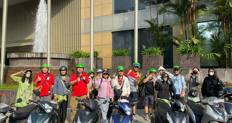 Grupo de turistas en scooters frente a un edificio, llevando cascos verdes.
