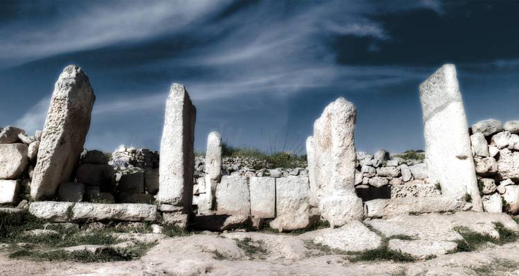 Antike Steinruinen vor einem dramatischen bewölkten Himmel, die eine Szene voller historischer Bedeutung schaffen.