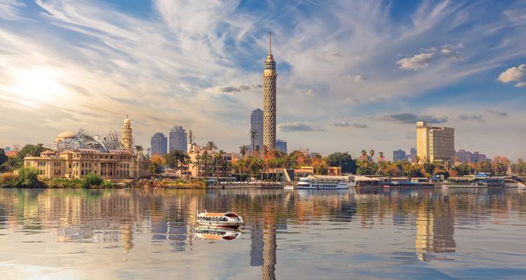 Cairo Tower and city skyline reflecting in the calm waters of the Nile at sunrise.
