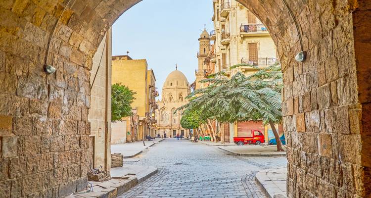 Stone archway framing a quiet cobbled street leading to a domed mosque in historic Cairo.