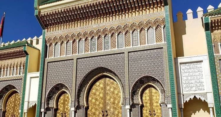 Golden ornate doors and detailed tilework of the Royal Palace gate gleam under a blue sky.
