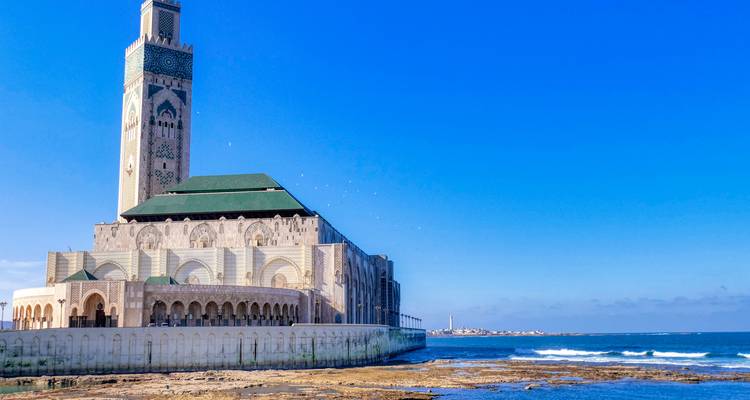 The Hassan II Mosque rises majestically over the Atlantic coast under a clear blue sky.