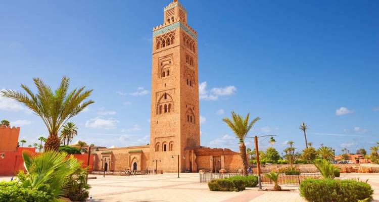 The Koutoubia Mosque minaret towers over palm-lined gardens under a bright blue sky.