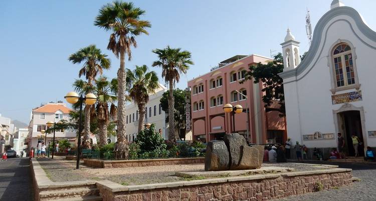 Place de ville bordée de palmiers avec des bâtiments coloniaux pastel et une petite église à Mindelo.