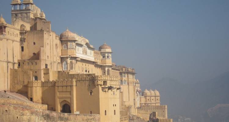 Verschwommener Blick auf die gelbockerfarbenen Wälle und Kuppeln des Amber Fort, die sich entlang eines Bergrückens erstrecken.