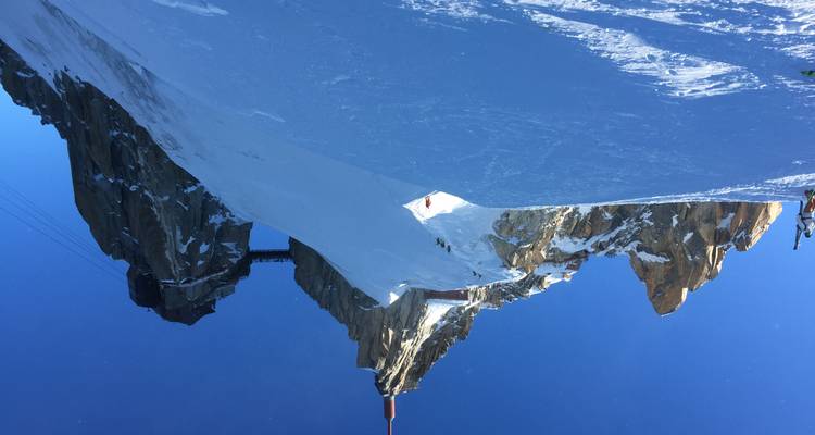 Une crête enneigée mène à la station du sommet de l'Aiguille du Midi sous un ciel alpin d'un bleu profond.