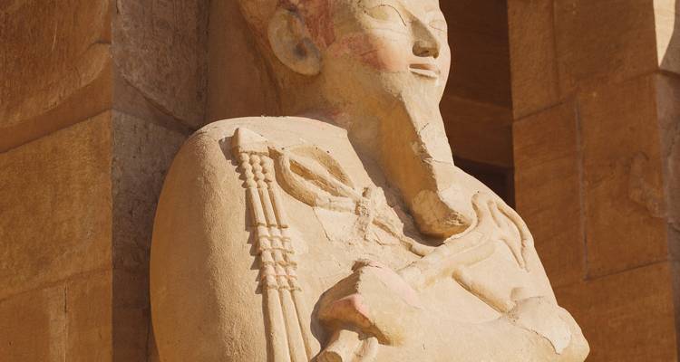 Close-up of a weather-worn sandstone pharaoh statue carved into a temple wall.