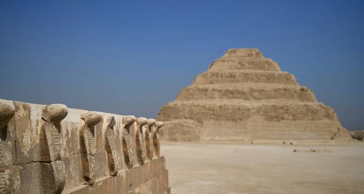 The Step Pyramid of Djoser rises from the sandy plateau with cobra-headed stone fence in front.