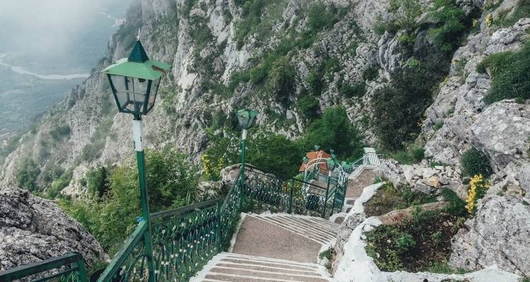 Escalier de montagne abrupt avec des rampes vertes surplombant une falaise de vallée brumeux.