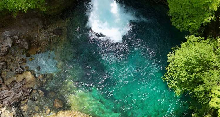 Vue de dessus d'une puissante cascade se jetant dans un bassin d'eau émeraude cristalline entouré de verdure.