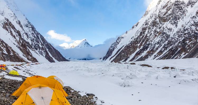 Reihen von gelben Expeditionszelten stehen neben einem riesigen schneebedeckten Tal, das von steilen eisigen Wänden flankiert wird.